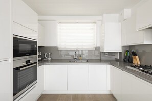 Uma cozinha moderna com armários brancos, forno embutido, fogão a gás e janela com persianas.
