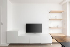 Ein modernes Wohnzimmer mit einem Flachbildfernseher an einer weißen Wand, einem Holzessttisch und eingebauten weißen Schränken.