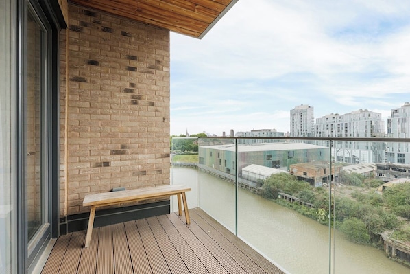 Ein Balkon mit einer Holzbank, einer Ziegelwand und Blick auf einen Fluss und Gebäude.