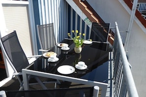 A dining table set with plates, cups, and a vase of yellow flowers on a balcony with metal railings and a view of the building's exterior. - in the Boddenblick house, Apt. 32 (Zingst)