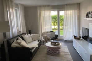 A modern living room with a black sofa, a white coffee table, and a television on a white cabinet. - Holiday apartment with 1 bedroom (Kühlungsborn)