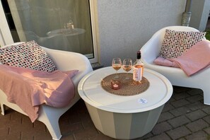 Two white chairs with patterned cushions, a round table with a bottle and glasses, and a glass door in the background. - Holiday apartment with 1 bedroom (Kühlungsborn)