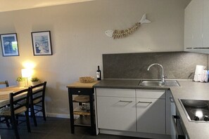A compact kitchen with a sink, stove, and a small dining area with chairs and a table. - Holiday apartment with 1 bedroom (Kühlungsborn)