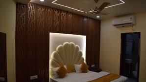 Una habitación de hotel moderna con una cabecera de cama original, un ventilador de techo, un equipo de aire acondicionado y una puerta de baño visible.