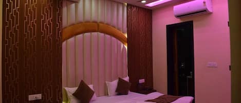A bedroom with a bed, bedside tables, a ceiling fan, an air conditioning unit, and a door.