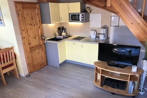 Eine kompakte Küche mit Mikrowelle, Kaffeemaschine und einem Fernseher auf einem Holzbalken.