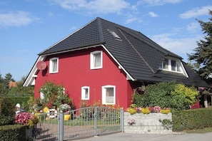 Ein rotes Haus mit schwarzem Dach, weißen Fenstern und einem Metallgitter.