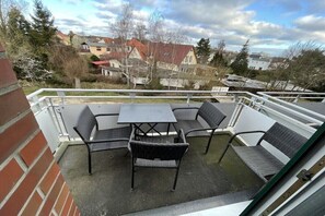 Ein Balkon mit Tisch und Stühlen, eine Ziegelwand und Blick auf Häuser und Bäume.
