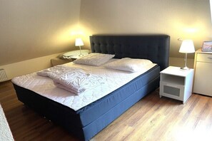 Ein Einzelbett mit dunklem Kopfteil, zwei Nachttische mit Lampen und ein kleiner Beistelltisch ebenfalls mit einer Lampe.