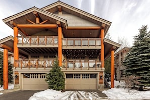Eine mehrstöckige Blockhütte mit Balkon, Garage und schneebedecktem Gelände.