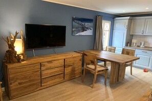 A modern kitchen with white cabinets, a wooden dining table, and a flat-screen TV mounted on the wall. - Holiday apartment with 2 bedrooms (Zingst)