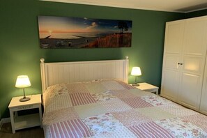 A bedroom with a bed, two bedside tables with lamps, a large painting above the bed, and a wardrobe. - Holiday apartment with 2 bedrooms (Zingst)