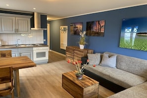 A modern kitchen with white cabinets, a wooden dining table, and a grey sofa in a living area with artwork on the wall. - Holiday apartment with 2 bedrooms (Zingst)