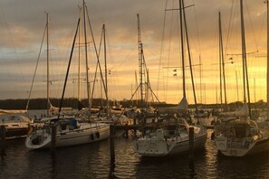 Ein Yachthafen mit mehreren Segelbooten, ruhigem Wasser und einem Sonnenuntergang im Hintergrund.