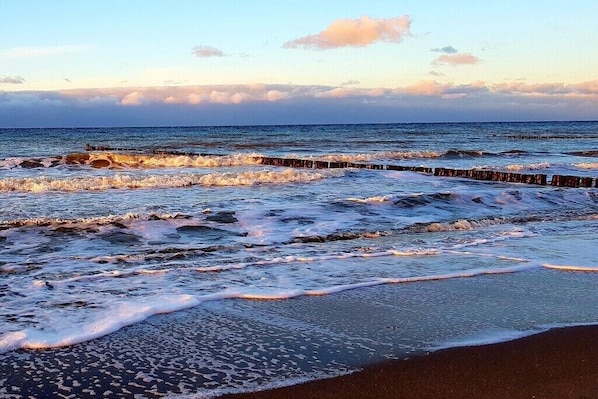 Ein Strand mit Wellen, einem hölzernen Wellenbrecher und blauem Himmel.