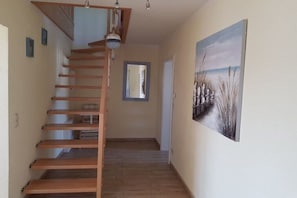 Eine Treppe mit Holzboden und Handlauf, ein Gemälde mit Strandmotiv und ein Spiegel an der Wand.