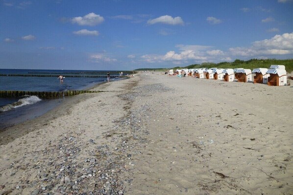 Ein Strand mit Kieselsteinen und Sand, mit einer Reihe Strandkörben und Streifenmarkisen.