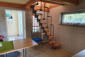 Une cuisine avec une table en bois, une chaise bleue, un radiateur et une fenêtre donnant sur un paysage verdoyant.
