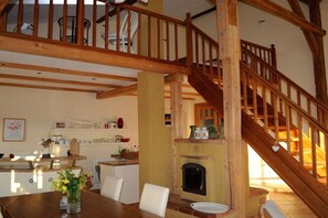 Ein geräumiges Zimmer mit einer Holztreppe, einem Kamin und einem Essbereich mit Tisch und Stühlen.