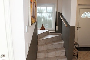 Eine Treppe mit Handlauf, ein Fenster mit Ausblick und eine Tür mit geometrischem Muster.