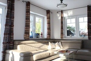 Ein Wohnzimmer mit einem beigefarbenen Sofa, einem Couchtisch und einem Fenster mit Vorhängen.