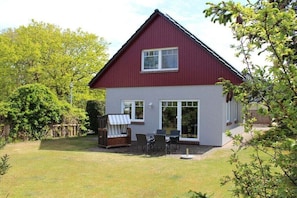 Ein Haus mit rotem Dach und weißer Fassade, eine Terrasse mit Gartenmöbeln und einem eingezäunten Garten.