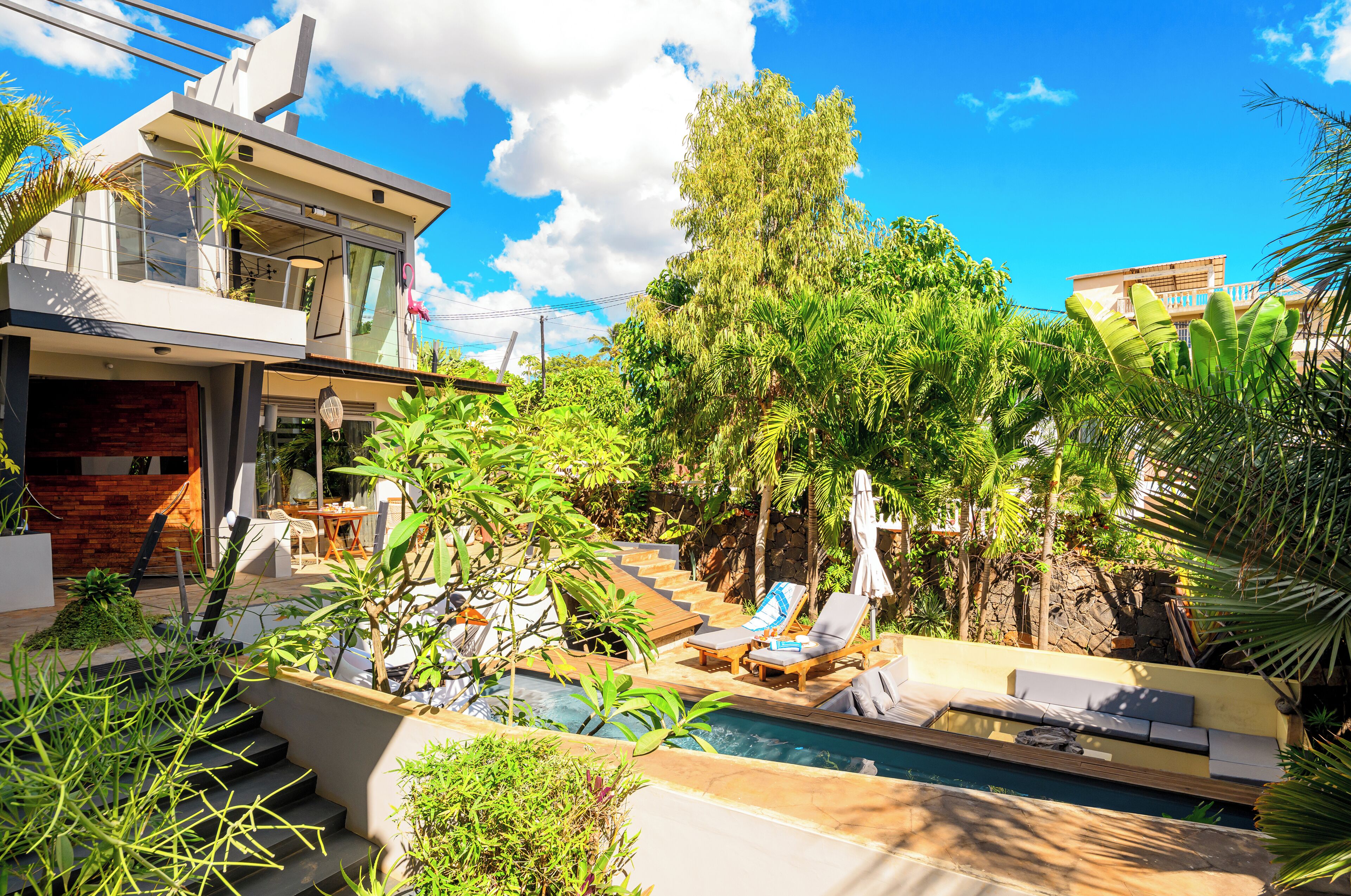 A modern house with a swimming pool, lounge chairs, and a staircase leading to a balcony.