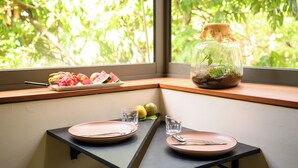 Zona pranzo con tavolo apparecchiato per due, una finestra vista sul verde e un terrario in vetro sul davanzale.