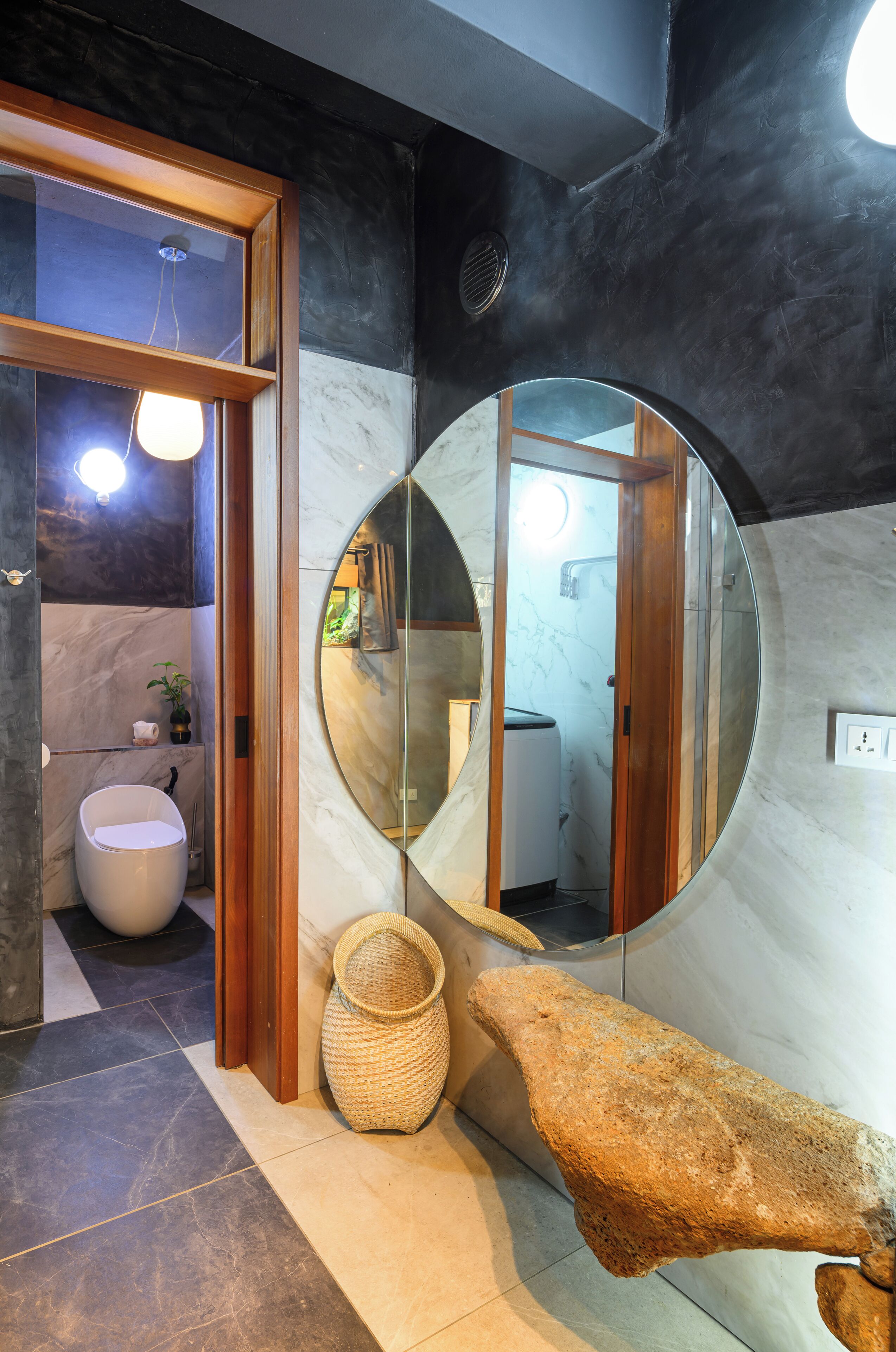 Een moderne badkamer met een ronde spiegel, een witte wastafel en een stenen bankje.
