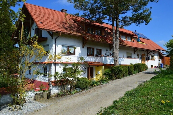 Ein traditionelles, zweistöckiges Haus mit rotem Ziegeldach, einem sichtbaren Schornstein und einem Weg zum Eingang.