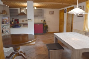 Ein Essbereich mit Holztisch und Bank, eine Küche im Hintergrund und eine weiße Wand mit einem gerahmten Bild.