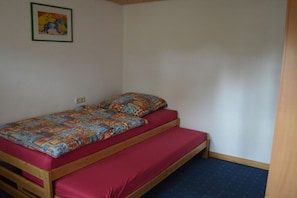Ein Einzelbett mit einer bunten Steppdecke und roter Bettwäsche in einem Zimmer mit weißen Wänden und einem blauen Teppich.