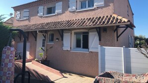 Ein zweistöckiges Haus mit einem Ziegeldach, weißen Fensterläden und einer kleinen Veranda.