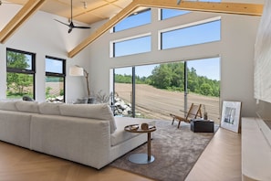 A spacious living room with a high ceiling, large windows, a sofa, a side table, and a painting. - Koi by H2 Life (Niseko)