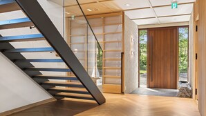 A modern interior with a wooden staircase, a glass door leading outside, and a wooden floor.