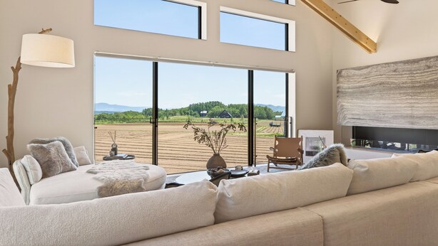 A spacious living room with a large window, a fireplace, and a ceiling fan.