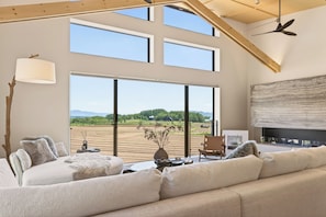 A spacious living room with a large window, a fireplace, and a ceiling fan. - Koi by H2 Life (Niseko)