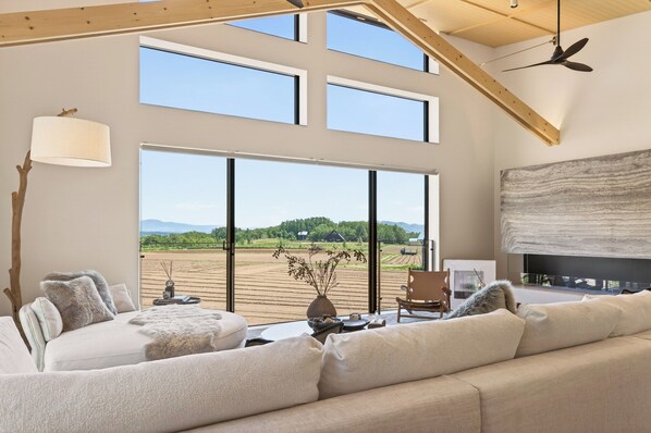 A spacious living room with a large window, a fireplace, and a ceiling fan.