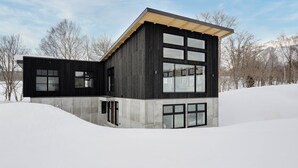 A modern building with a dark exterior, large windows, and a sloped roof.