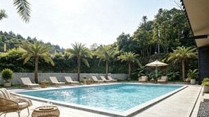 A rectangular pool with lounge chairs and a table, surrounded by a stone wall and palm trees.