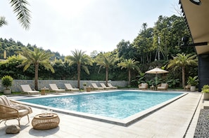 A rectangular pool with lounge chairs and a table, surrounded by a stone wall and palm trees.