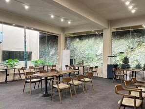 Ein Konferenzraum mit mehreren Tischen und Stühlen, großen Fenstern und einer Wand aus Stein.