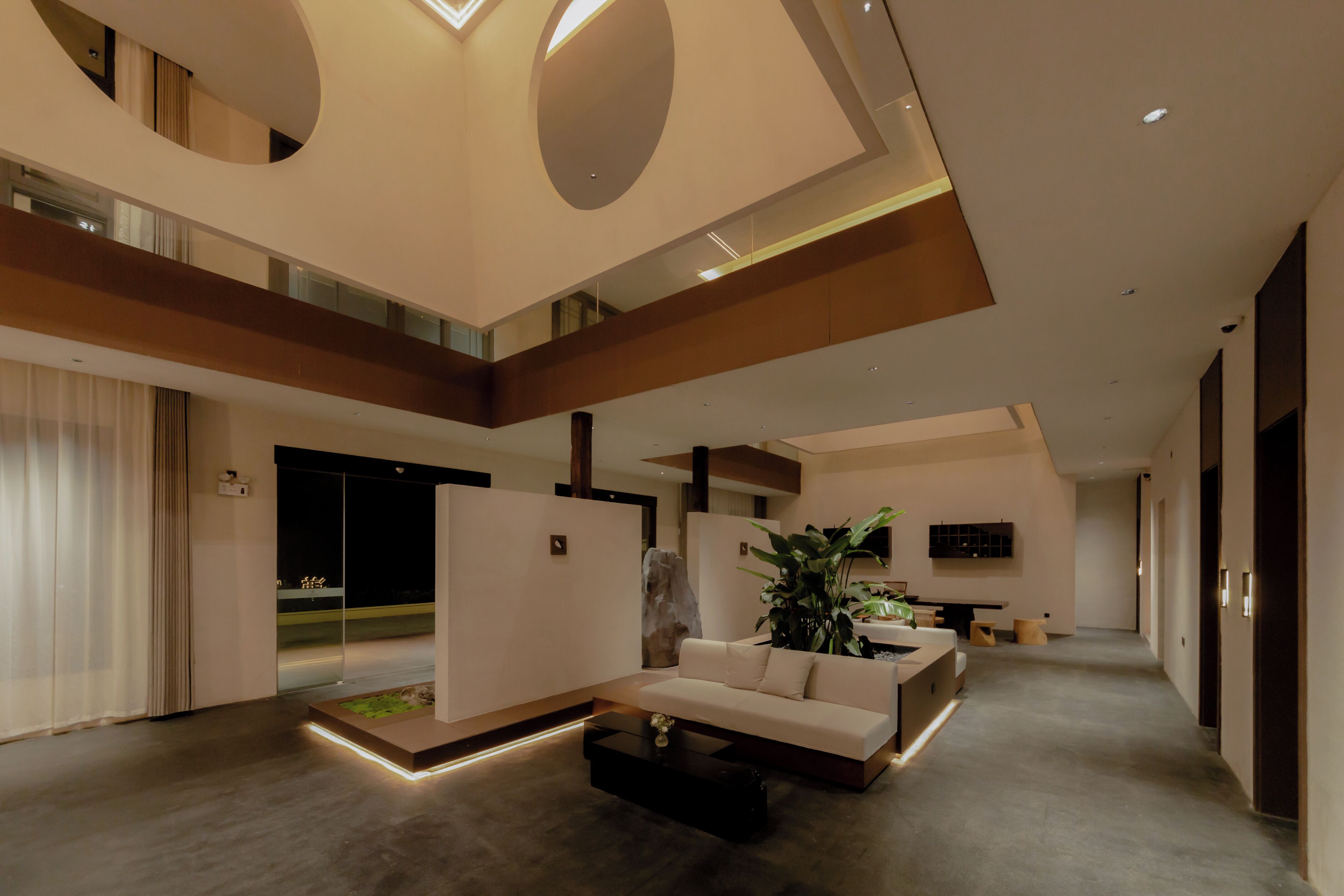 Un interior moderno con una zona de estar central, una escalera y una planta grande.