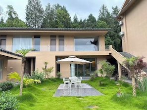 A two-story building with a balcony, a covered patio with a table and chairs, and a staircase leading to the upper floor.