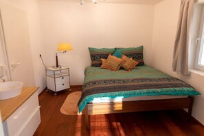 A bedroom with a bed, bedside table, lamp, and a window with curtains. - Holiday apartment with 2 bedrooms (Unteruhldingen)