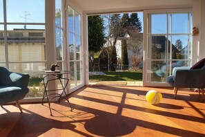 A room with large windows, a wooden floor, a round table, two chairs, and a yellow ball. - Holiday apartment with 2 bedrooms (Unteruhldingen)
