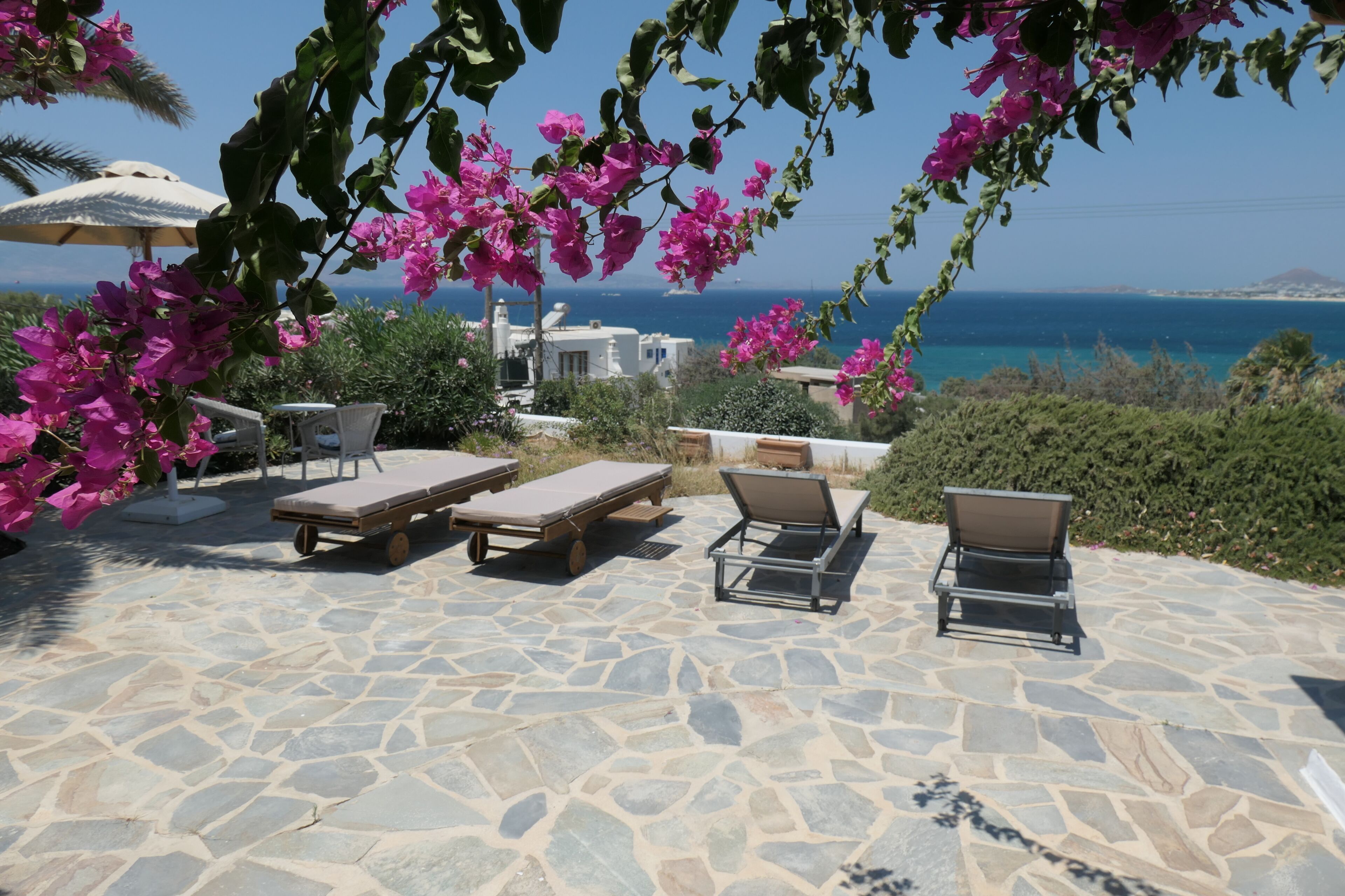 A stone patio with lounge chairs and a view of the sea.