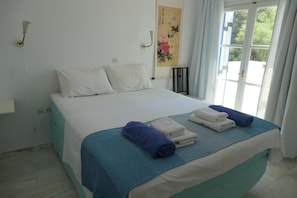 A hotel room with a bed, a window with curtains, and a wall-mounted light fixture. - Charming Naxos Villa, Ocean Views, Modern Comfort, Tranquil Escape (Naxos)