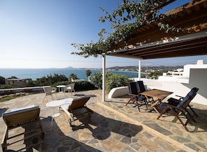 Eine Terrasse mit Steinboden, Gartenmöbeln und Blick auf das Meer.