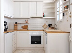 Una cucina compatta con mobili bianchi, forno a incasso, macchina da caffè e piano di lavoro in legno.